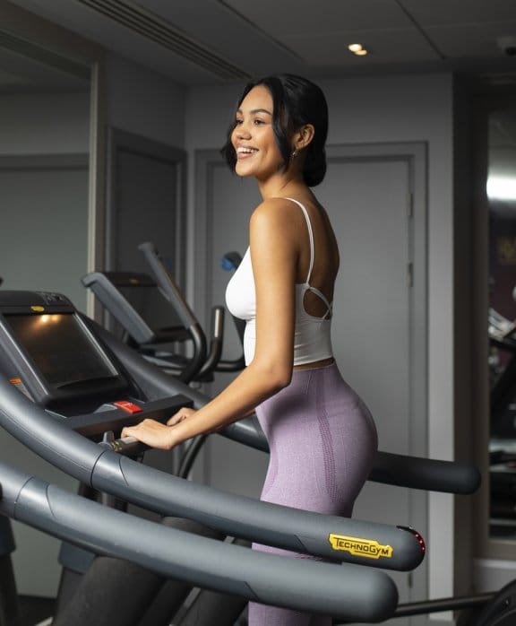 A woman in sports gear smiles and works out on a treadmill