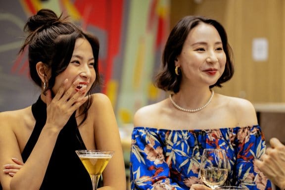 Two girls holding their laughter over a cocktail and a glass of wine