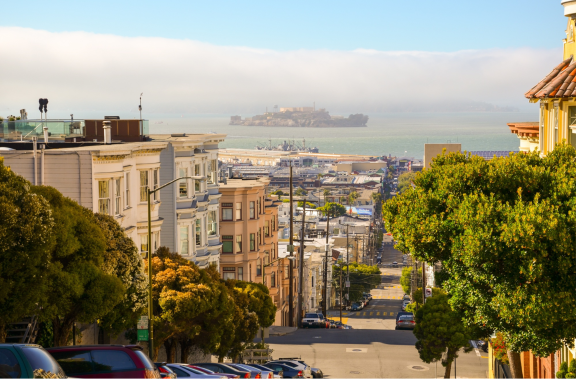 A bright street-view scene of suburban San Francisco with Alcatraz seen in the distance