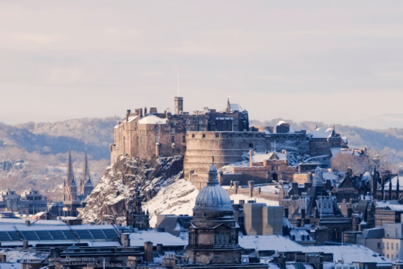 Edinburgh Castle in the snow with Arthur's Seat mountain behind 