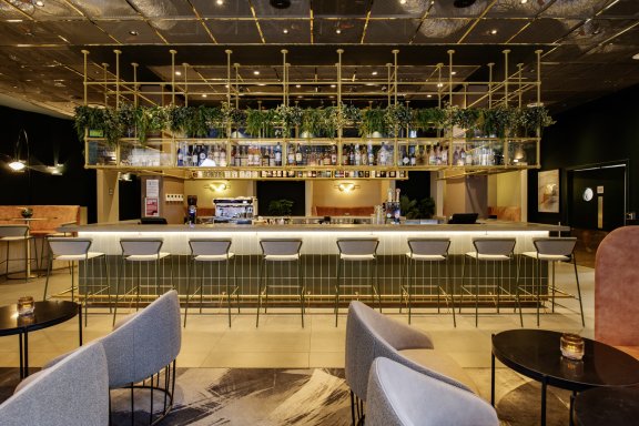 A trendy bar with mood lighting, white seats and leafy decor