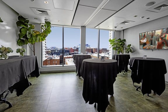 Five round tables set out in a large room with floor-to-ceiling windows and a big TV screen