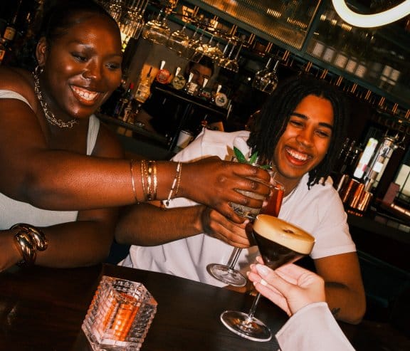 A group of friends clinking glasses in a vibrant, dimly lit bar