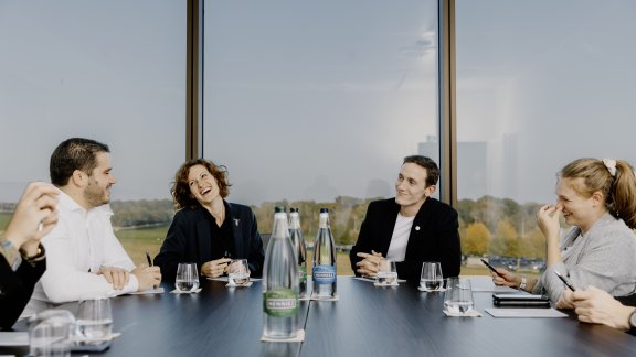 Four people sitting round a boardroom table, laughing 