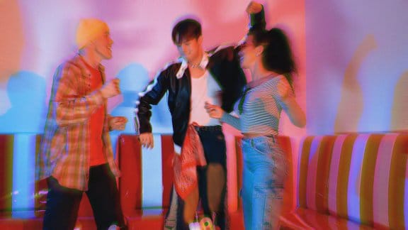 Three people dancing in a vibrant room lit up with reds and pinks