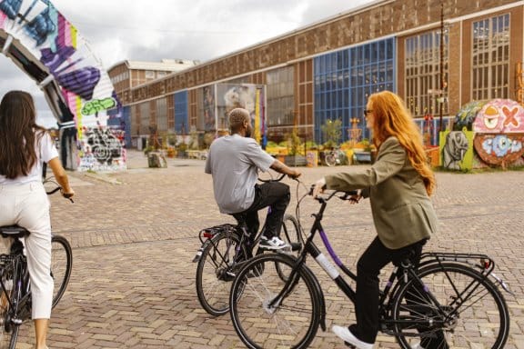 Three people cycling through an eclectic street in Amsterdam