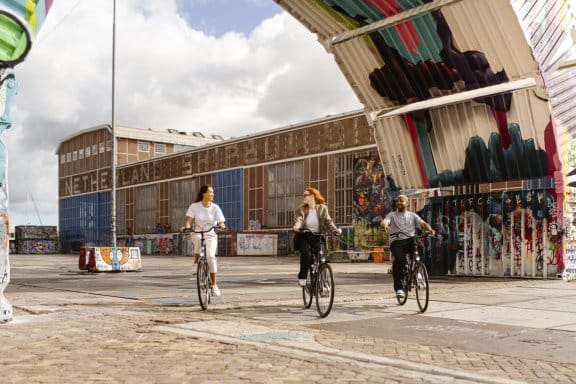 Three people cycling through an eclectic street in Amsterdam