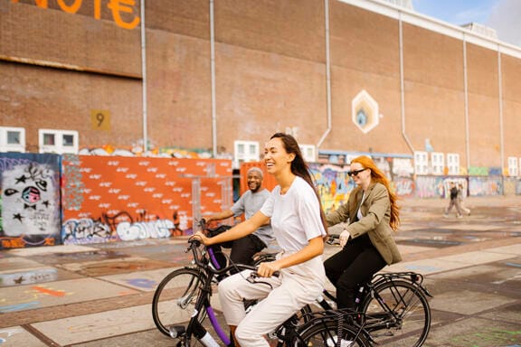 Three people cycling through an eclectic street in Amsterdam