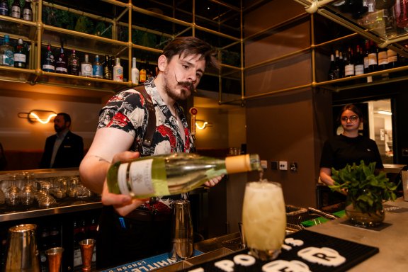 A bartender with an impressive moustache prepares a cocktail in a performative fashion