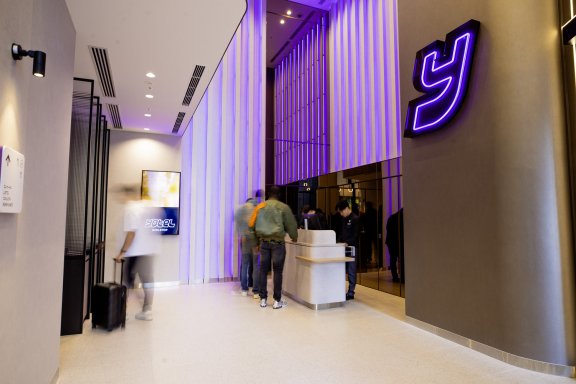 Clean hotel lobby with white floors and purple panneling. The Y Yotel logo hands luminescent on the wall