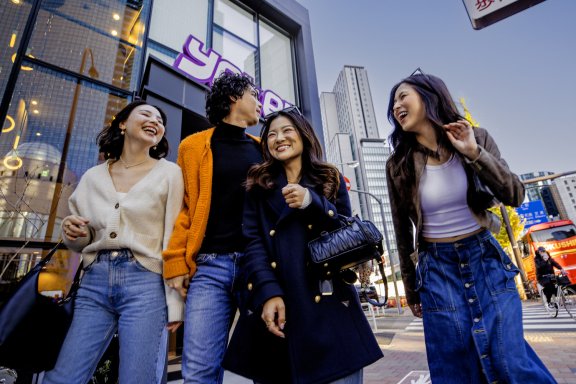 Four friends gather and laugh outside the modern glass facade of YOTEL Tokyo