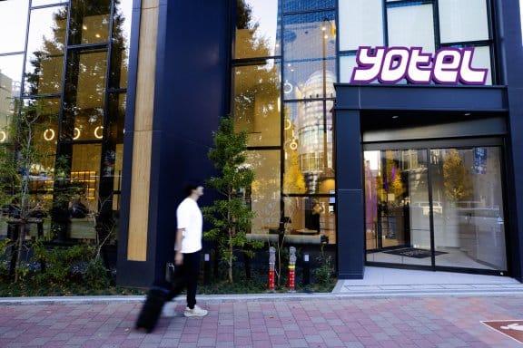 A man walks up to a glamorous lobby entrance to YOTEL, a smart modern hotel with a large glass foyer
