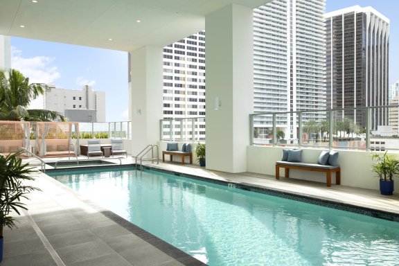 A high-rise swimming pool with sun loungers with Downtown Miami in the background