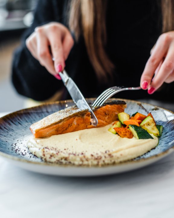 A lady cutting into a salmon fillet