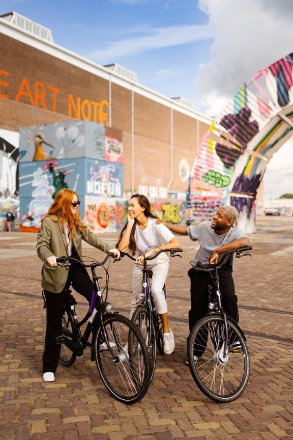 Three people cycling through an eclectic street in Amsterdam