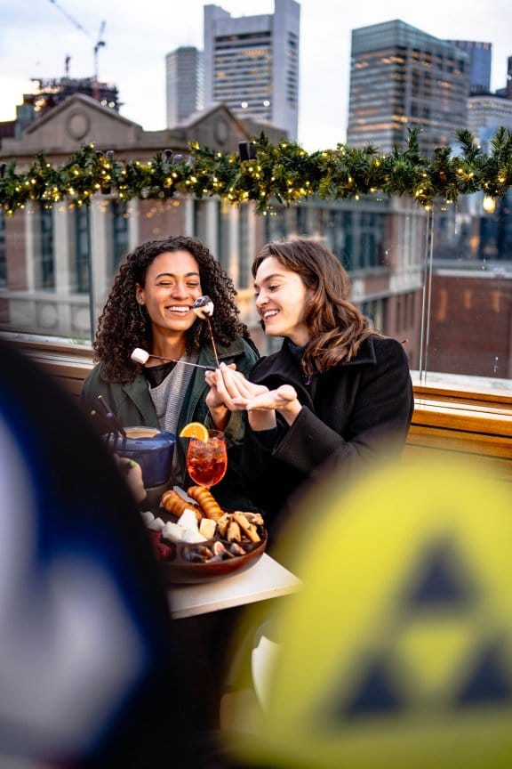 Two friends enjoy apres and cocktails at a rooftop hotel bar