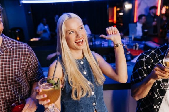A woman in a bar laughs with a cocktail