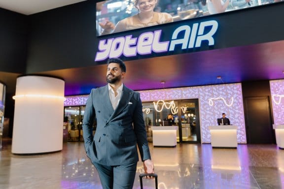A well-dressed man rolls his suitcase outside an airport hotel facadei it reads YOTELAIR