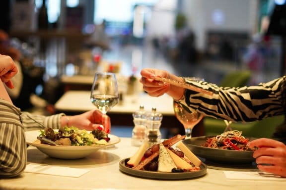 Two people in shirts enjoy a glass of wine and a meal at a fancy restaurant