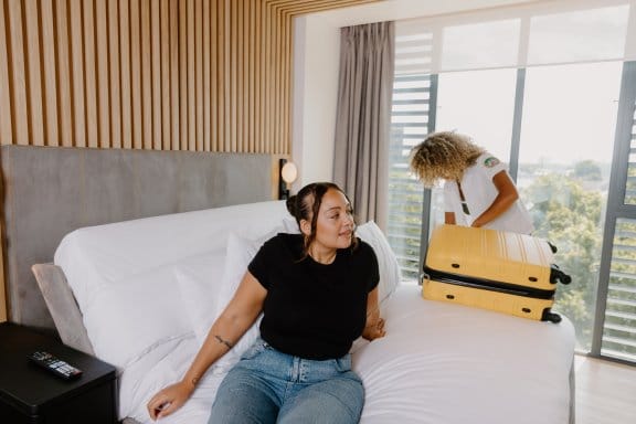 Two women unpacking their suitcase in a bright hotel room bed
