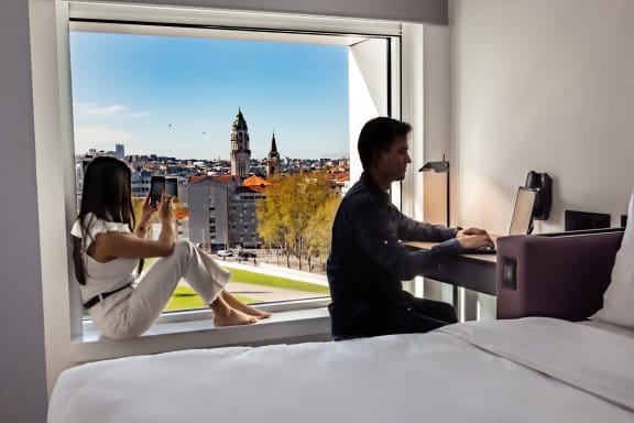 A man and a woman look out their hotel window at a Porto landscape 