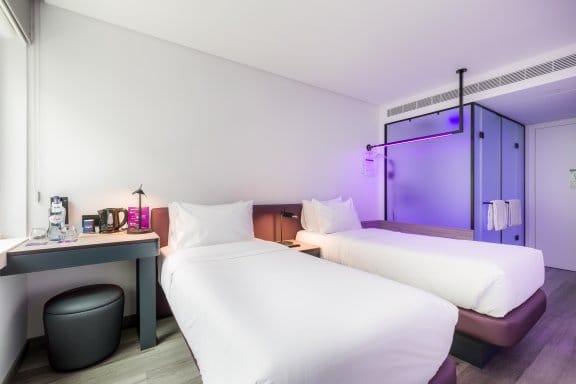 Hotel guest room depicting two single beds and purple glass bathroom