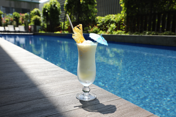 A fruity cocktail sitting by the poolside with a leafy background