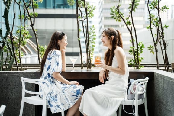 Two girls chat over cocktails next to an outdoor hotel pool 
