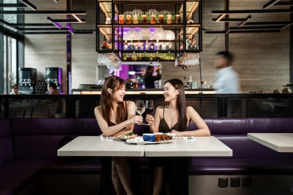 Two woman click their glasses over a meal in a trendy hotel restaurant and bar