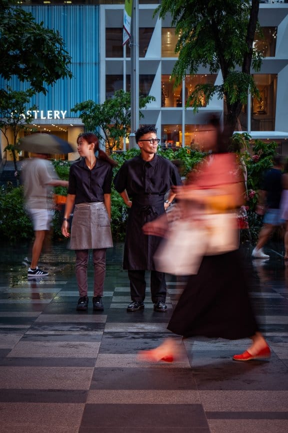 Two staff members stand to attention in an atmospheric outdoor hotel restaurant