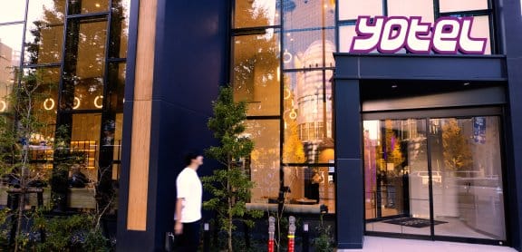 A man walks up to a glamorous lobby entrance to YOTEL, a smart modern hotel with a large glass foyer