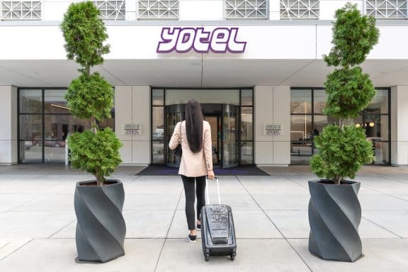A smartly dressed woman approaches a hotel lobby with her suitcase
