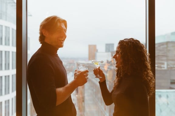 A man and a woman laugh and drink in front of huge floor-to-ceiling windows overlooking Glasgow