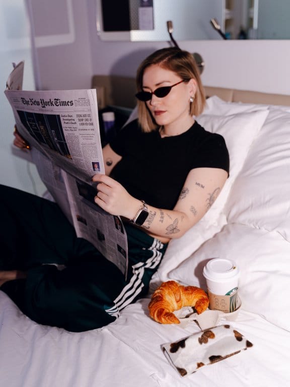 A hip girl reads a newspaper in her hotel room
