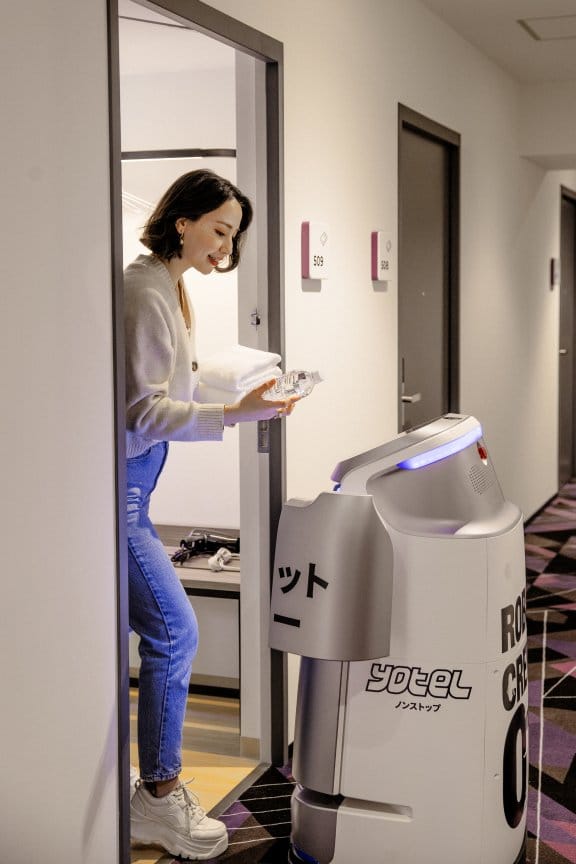 A woman greets a robot at her hotel room door