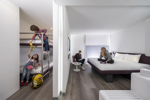 YOTEL Istanbul Airside family room with parents relaxing on double bed and kids playing on bunk beds separated by a wall