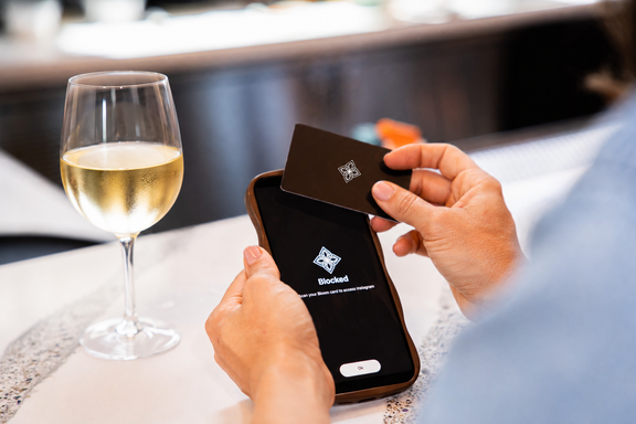 A man taps a card to his mobile photo with a glass of white wine