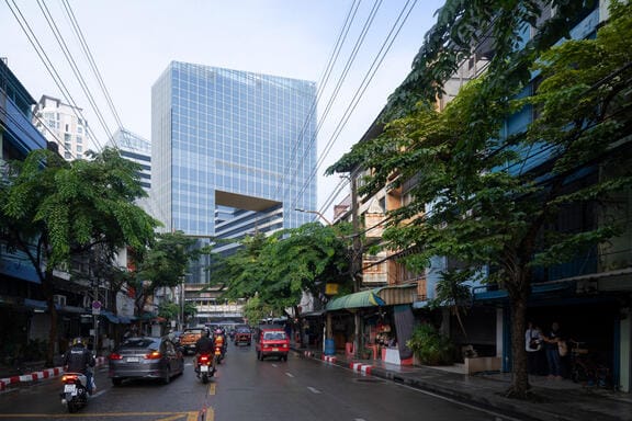 A modern glass building at the end of a tree-lined street