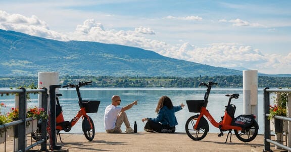 Two people sitting on a deck overlooking a lake and mountains with bikes in the foreground
