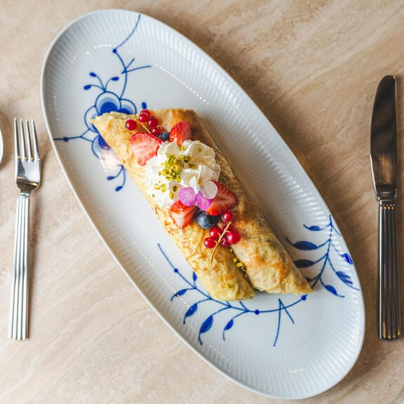 An elegant breakfast served on a patterned oval plate with generous dressings
