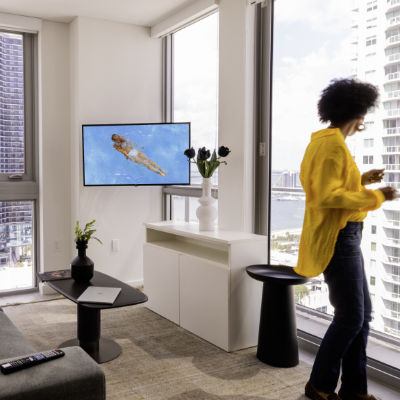 A woman in a yellow top looks out the window from her studio pad lounge area