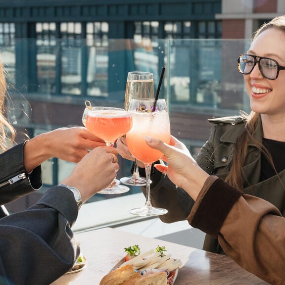 Two women clinking their glasses on a bright rooftop bar
