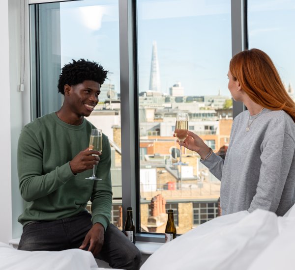 Man and woman holding a glass of champagne looking out of hotel window
