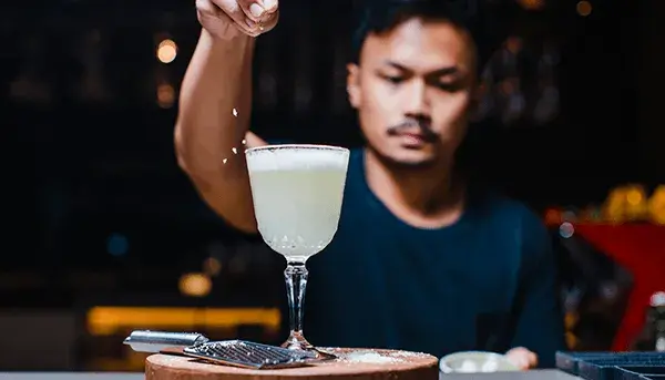 A man with a moustache adds a sprinkle of seasoning to a cocktail 