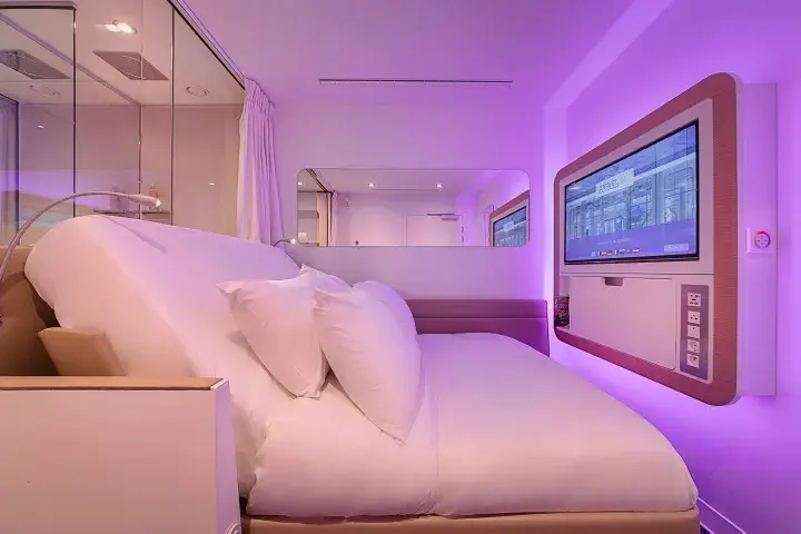 A Queen-sized cabin with purple light and a bed raised up to allow a comfortable view of the television