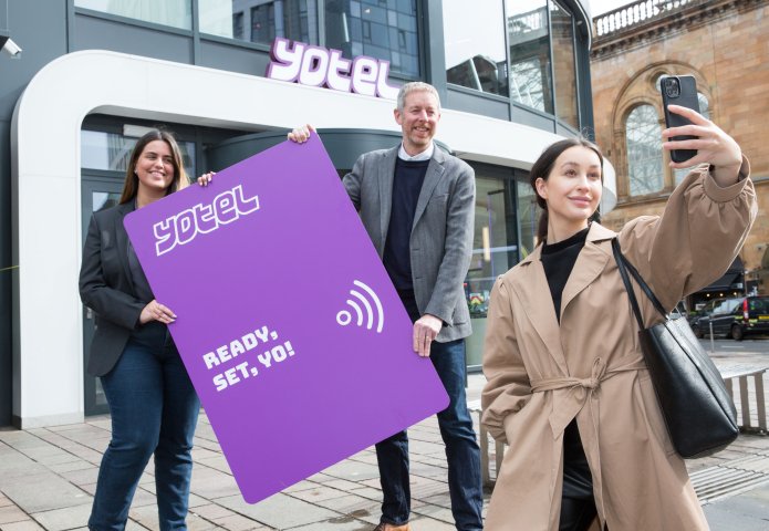 Hotel staff holding large purple key card in front of YOTEL Glasgow. 