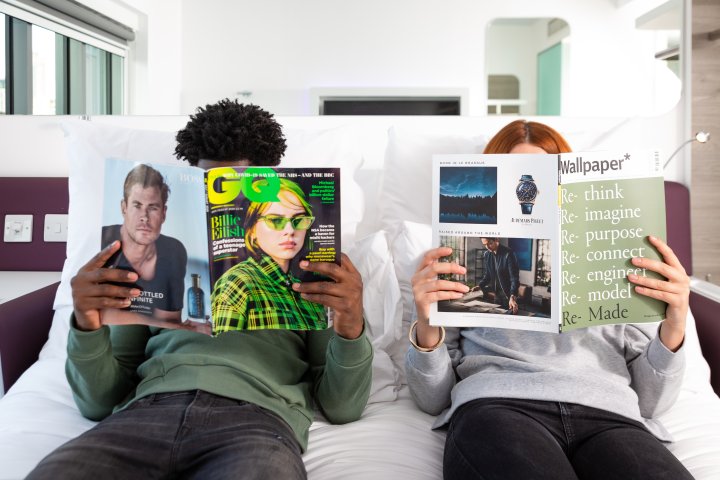 Two people sitting on a bed reading magazines