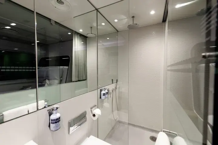 A hotel room bathroom with a large mirror, folded towels, sink, and rainshower