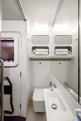 A hotel room bathroom with a large mirror, folded towels, sink, and rainshower