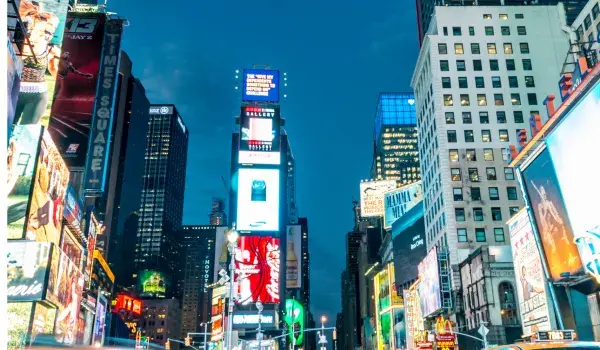 A buzzing view of times square, surrounded by speeding yellow taxis at night